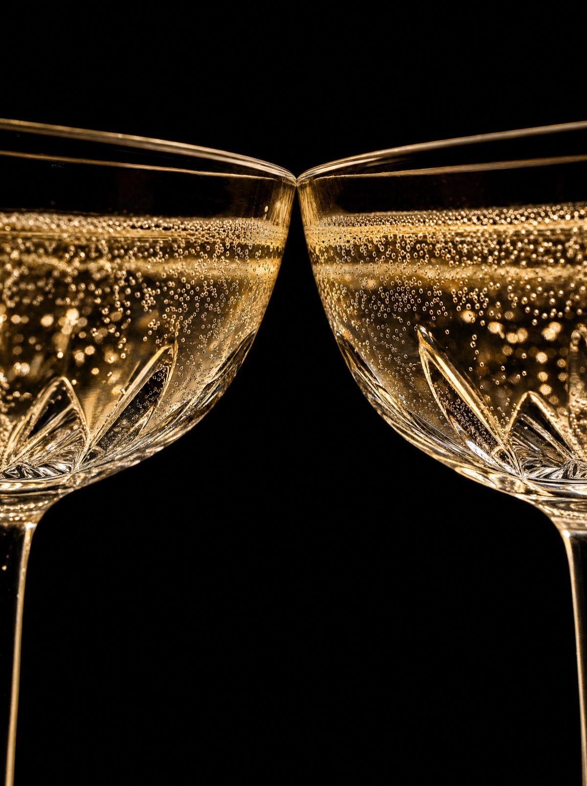 A toast: the rims of two glasses of sparkling wine in golden light