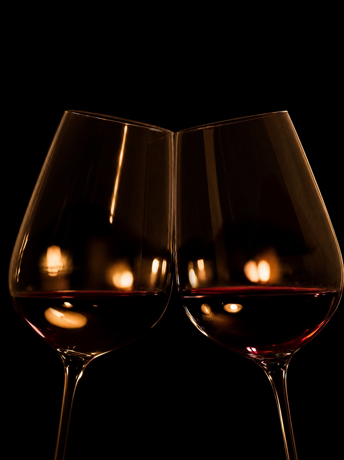 Two glasses of red wine touching in a toast by candlelight