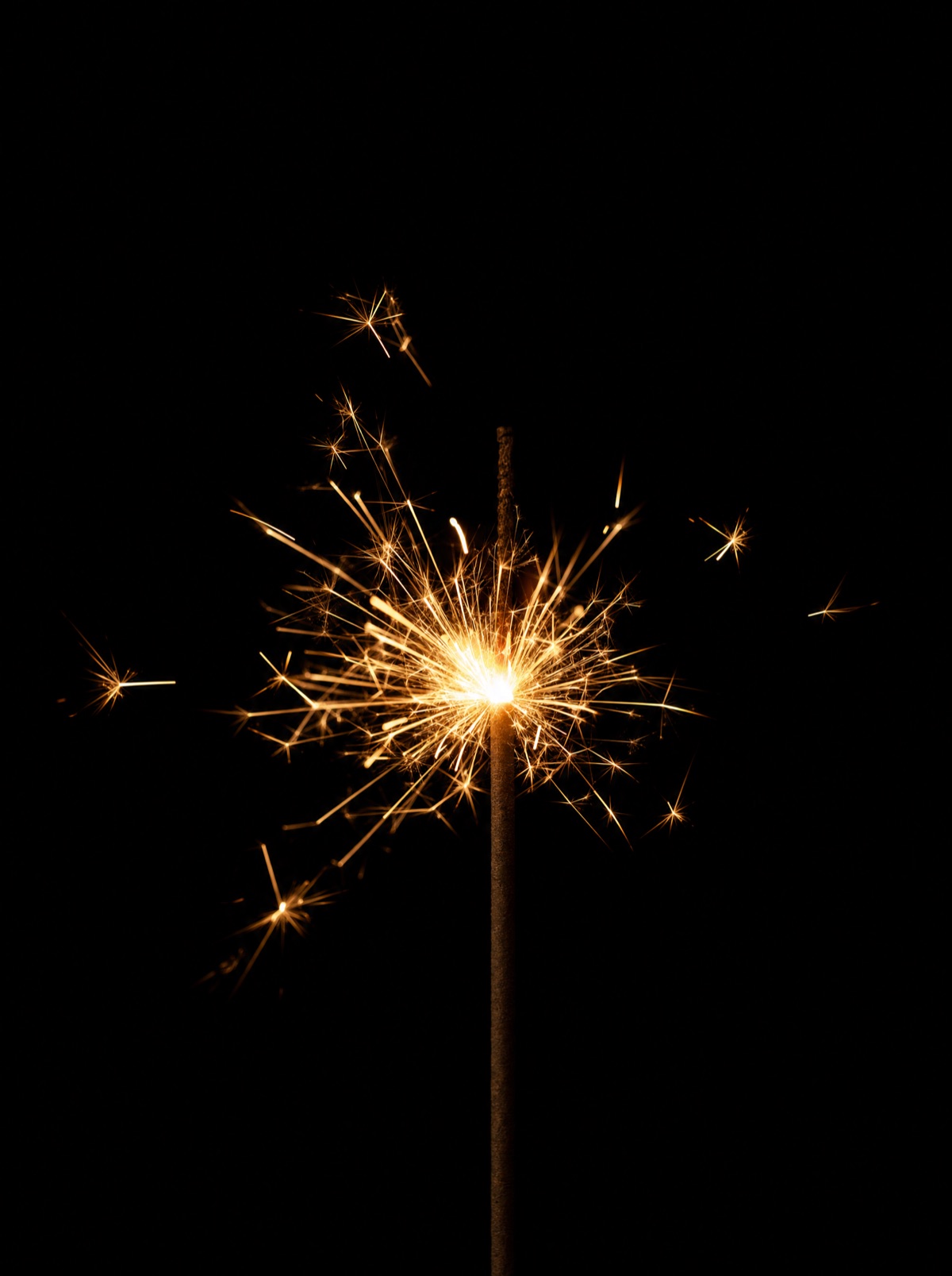 A sparkler against a black background, golden sparks